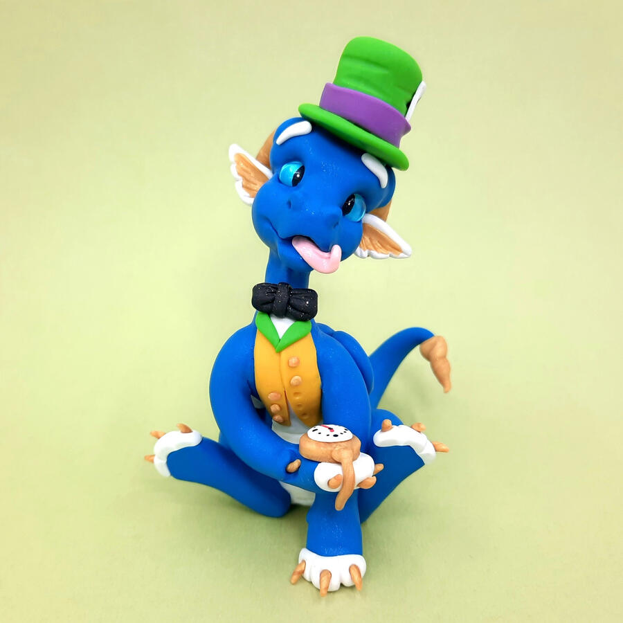A blue clay 'Mad Hatter' dragon faces the camera, holding a golden pocket watch in its paw. It is displayed in front of a green background. A blue clay 'Mad Hatter' dragon faces the camera, holding a golden pocket watch in its paw. It is displayed in front of a green background.